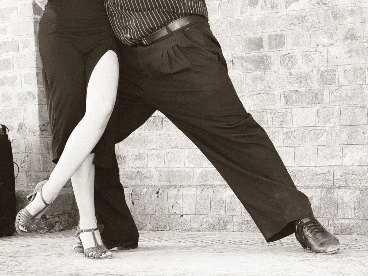 Close detail of a tango couple's footwork mid-step against a brick wall